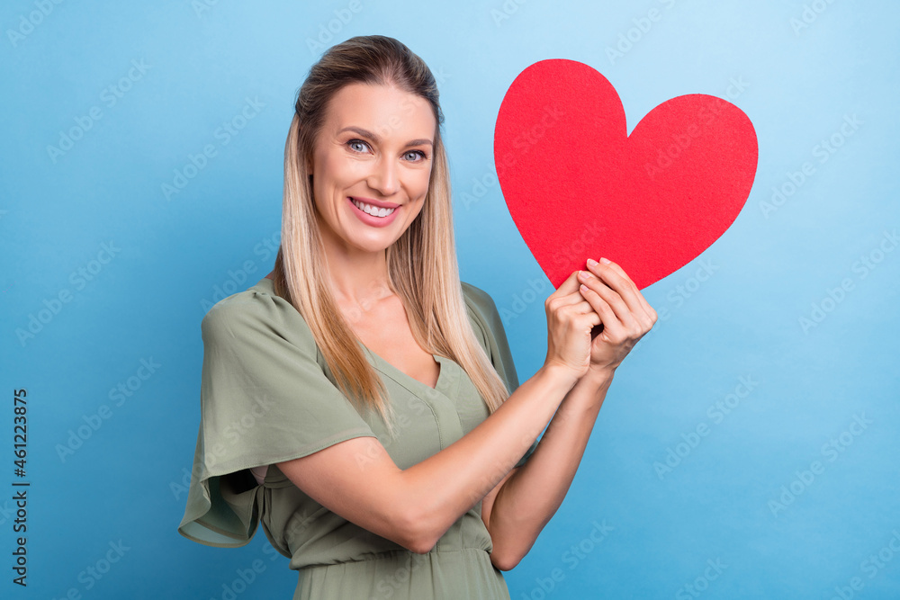 Photo of shiny cute young woman dressed green clothes holding hands arms large red heart card smiling isolated blue color background Photo of shiny cute young woman dressed green clothes holding hands arms large red heart card smiling isolated blue color background