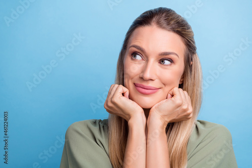 Photo of cute dreamy young woman dressed green clothes arms cheeks chin looking empty space smiling isolated blue color background