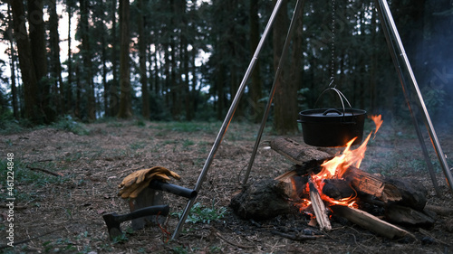 Fototapeta Naklejka Na Ścianę i Meble -  Camping outdoors in nature. Cooking pot hanging over a campfire on a tripod at a tourist camp, a bowler on a bonfire by firewoods. Preparing dinner in a pot in the forest. Nice camping background