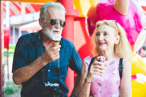 Portrait of loving and caring senior husband and wife on a vacation with a camera round the neck eating ice-cream while smiling and looking at camera