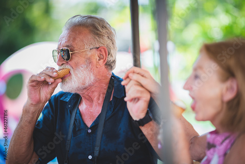 Portrait of loving and caring senior husband and wife on a vacation with a camera round the neck eating ice-cream while smiling and looking at camera