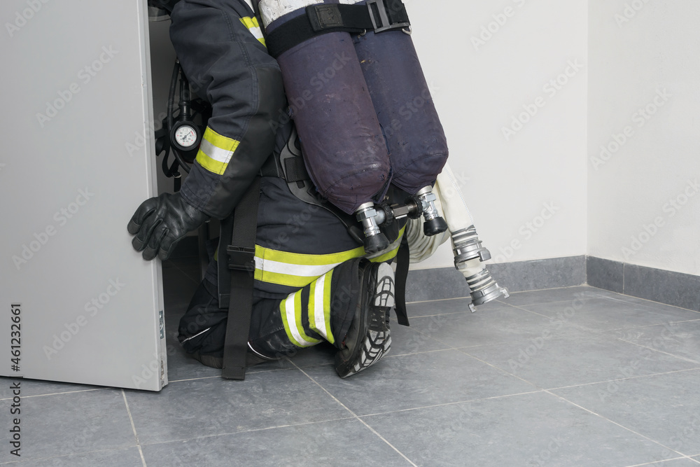a firefighter with equipment crawls through an open door to extinguish a fire in a building a firefighter with equipment crawls through an open door to extinguish a fire in a building