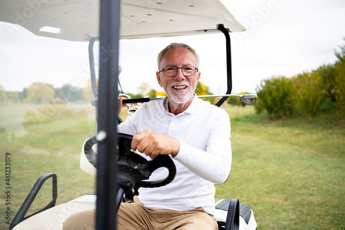 Portrait of wealthy senior golfer in golf car enjoying free time outdoors.