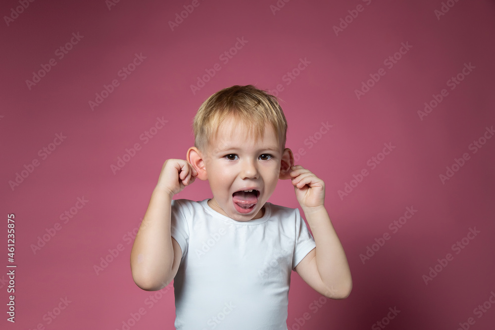 Caucasian boy makes faces, shows tongue, looking at camera on pink background Caucasian boy makes faces, shows tongue, looking at camera on pink background