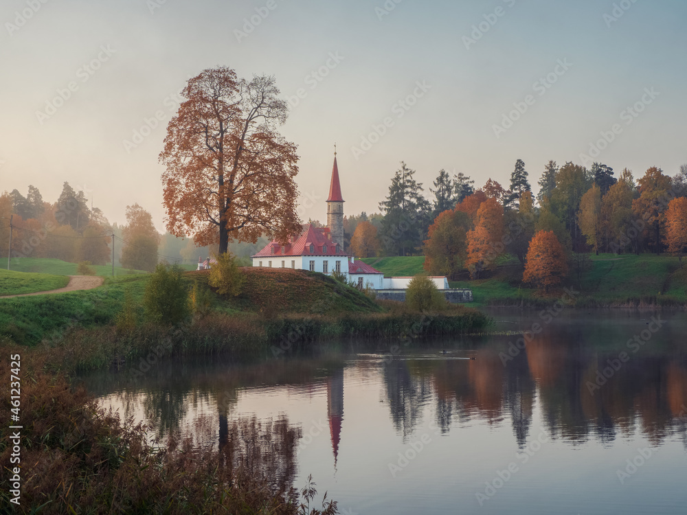 Sunny autumn morning landscape. A bright autumn misty landscape with golden trees by the pond and an old palace. Gatchina. Russia.