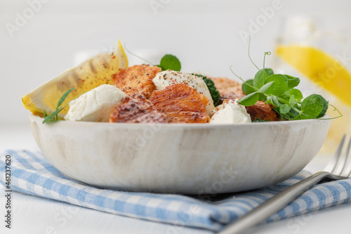 Baked salmon fillet salad with fresh vegetables, cream cheese, lemon, and microgreens.