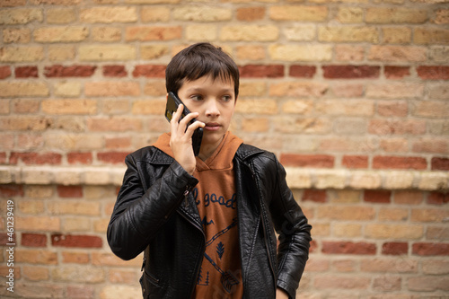 hoto of teenage boy aged 11-12 is talking on smartphone against background of brick wall in the city