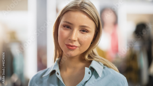 Portrait of Beautiful Young Woman with Light Blonde Hair and Green Eyes Wearing Jeans Shirt Looking Up to the Camera and Smiling. Successful Woman Posing for Camera. Blurred Clothing Store Background.