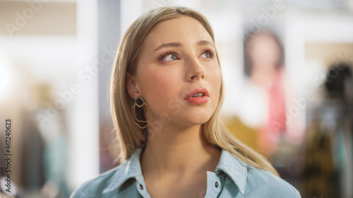 Portrait of Beautiful Young Woman with Light Blonde Hair and Green Eyes Wearing Jeans Shirt Looking Up. Successful Woman Posing for Camera. Blurred Clothing Store Background.