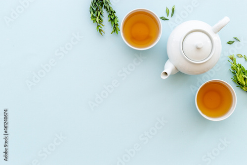 Tea drinking with white teapot and two cups with green leaves, top view