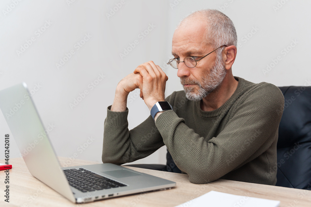 Adult, pensive man with gray hair working on laptop Adult, pensive man with gray hair working on laptop