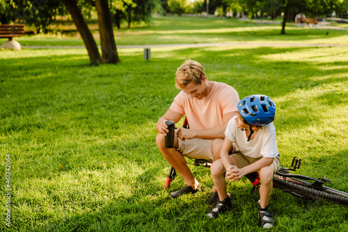 Ginger man and his son talking while sitting on bicycle in park