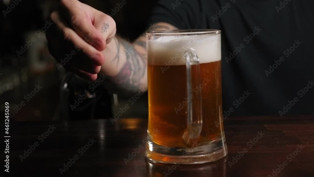 Close-up of a bartender putting a glass of light beer on the bar in a dark bar. The concept of alcohol and leisure.