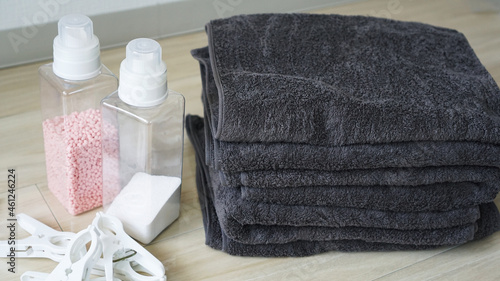 床に畳んで重ねられた洗濯物のタオルと洗剤、洗濯バサミのランドリーセット