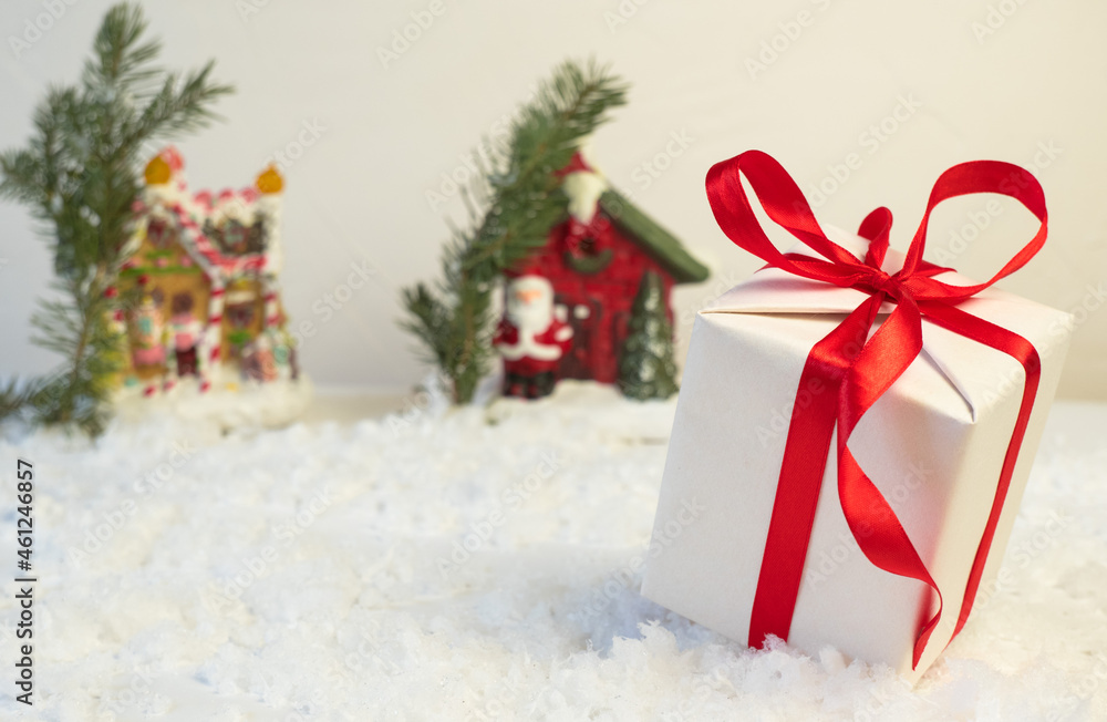 A gift box with a red ribbon lies on the snow. Christmas or New Year's gifts on the background of a snow-covered road, in the background houses and Christmas trees.