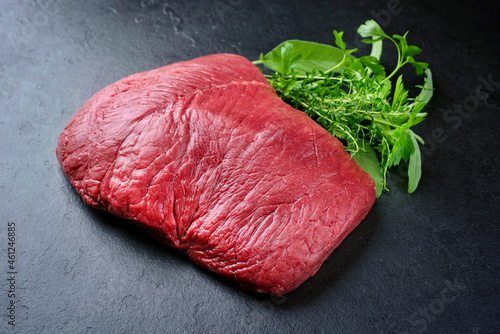 Raw dry aged bison beef rump steak piece as close-up with herbs on black background with copy space photo