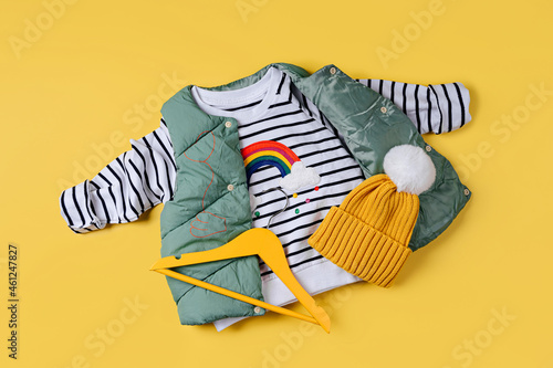 Waistcoat down jacket with striped jumper on yellow background. Stylish childrens outerwear. Fashion kids outfit. photo