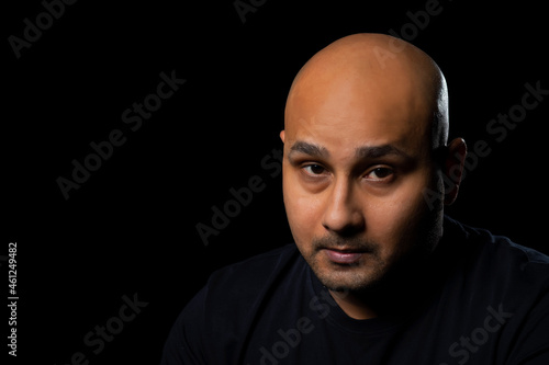 Portrait of a bald man looking at camera against dark black background.