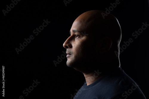 Portrait of a bald man with serious expression against dark black background.