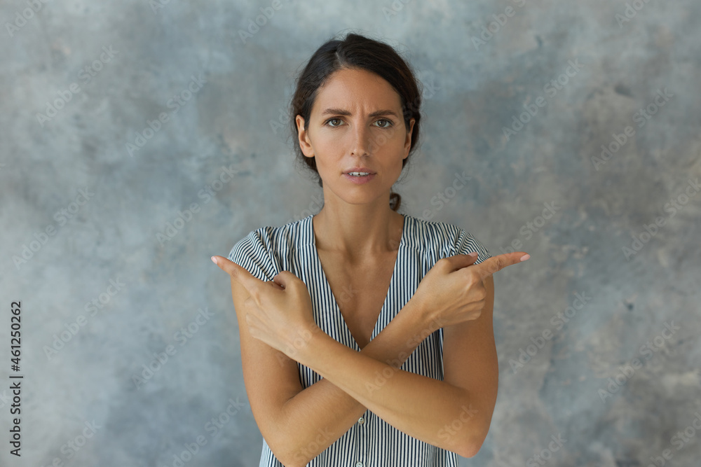 Indoor horizontal portrait of pretty woman in cute striped casual shirt frowning pointing at different sides with both index fingers, having puzzled face expression, trying to follow right direction Indoor horizontal portrait of pretty woman in cute striped casual shirt frowning pointing at different sides with both index fingers, having puzzled face expression, trying to follow right direction