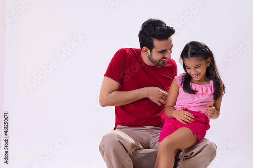 A FATHER SITTING AND TICKLING HIS DAUGHTER