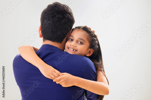 A YOUNG GIRL LOOKING AT CAMERA WHILE EMBRACING HER FATHER © IndiaPix