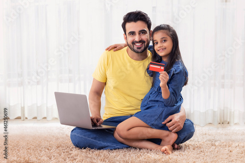 A DAUGHTER SITTING WITH FATHER LOOKING AT CAMERA WHILE HOLDING DEBIT CARD photo