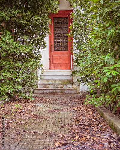 traditional family house external entrance door through dense green foliage garden.