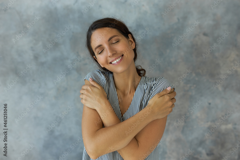 Self-love concept. Studio close-up portrait of smiling cute woman with dark hair hugging herself, giving herself love, support, respect, isolated against wall with copy space for advertising content Self-love concept. Studio close-up portrait of smiling cute woman with dark hair hugging herself, giving herself love, support, respect, isolated against wall with copy space for advertising content