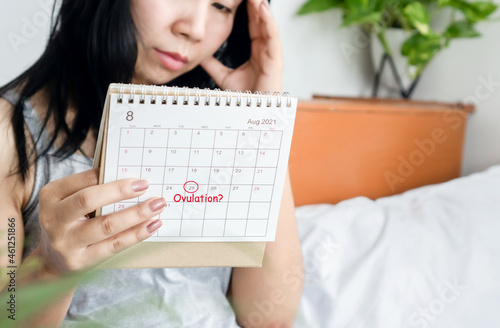 stressed Asian woman looking at  calendar having problem with menstrual cycle waiting for ovulation day photo