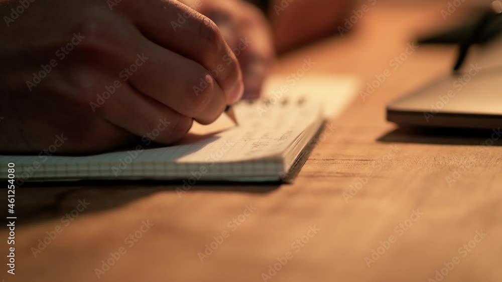 A close-up view of the male hands writing something in notepad in the office at night A close-up view of the male hands writing something in notepad in the office at night