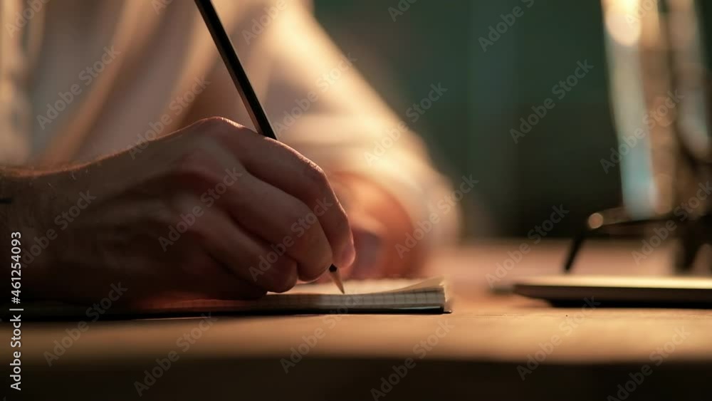A close-up view of the male hands writing something in notepad at the night