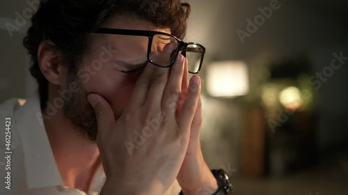 A side view of the man rubbing his eyes after work on laptop in the office at night