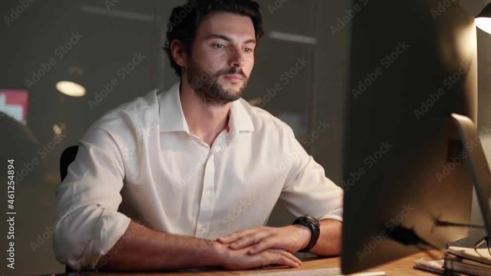 A concentrated handsome man typing on a wireless keyboard and looking with smile at the camera in the office A concentrated handsome man typing on a wireless keyboard and looking with smile at the camera in the office
