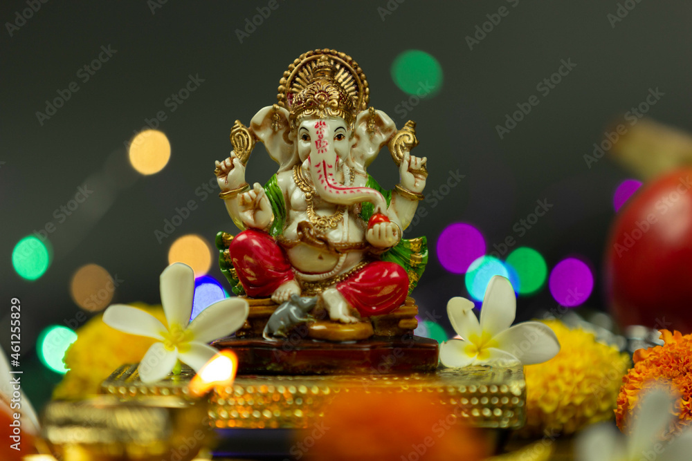 Front view of Statue Of Hindu God Ganesha Ganpati Sitting On Golden Asana With Fruits, Flowers, Lamp, shunkh And Blur Bokeh For Diwali Puja New Year Deepawali Ganesh Chaturthi Or Shubh Deepavali Pooja