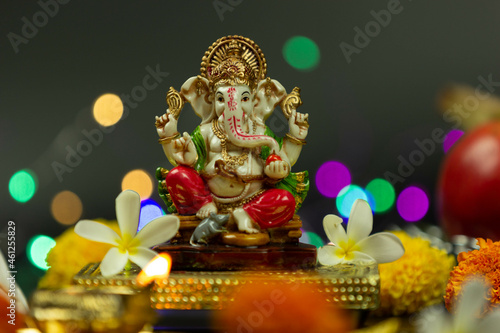 Front view of Statue Of Hindu God Ganesha Ganpati Sitting On Golden Asana With Fruits, Flowers, Lamp, shunkh And Blur Bokeh For Diwali Puja New Year Deepawali Ganesh Chaturthi Or Shubh Deepavali Pooja