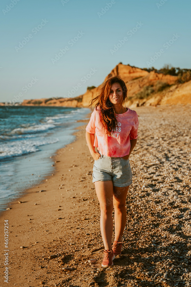 A young beautiful woman walks along the beach and admires the seascape at sunset
