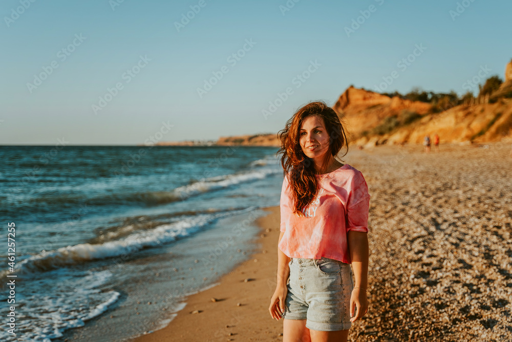 A young beautiful woman walks along the beach and admires the seascape at sunset