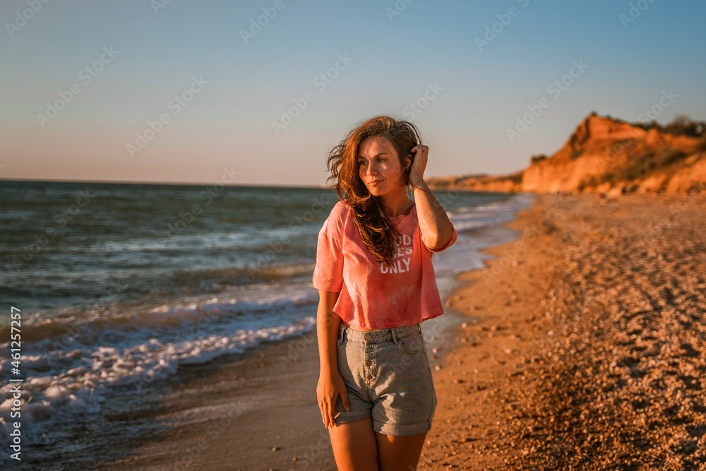 A young beautiful woman walks along the beach and admires the seascape at sunset