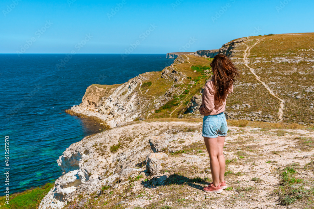 Rear view a young woman admires the picturesque seascape with azure water on the western coast of Crimea.