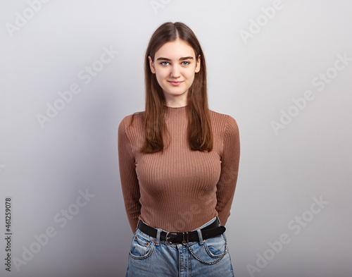 Pretty smiling thinking young natural woman with brunette long hair in casual dress looking happy. Studio shot of good looking beautiful woman isolated against grey studio wall