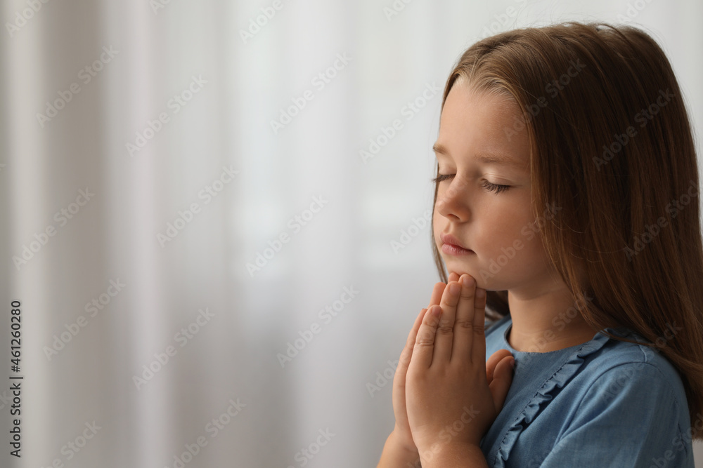 Cute little girl with hands clasped together praying indoors. Space for text Cute little girl with hands clasped together praying indoors. Space for text