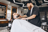 Portrait of professional barber, clipper cutting, shaving beard of regular customer at barbershop. Beauty, selfcare, style, fashion and male cosmetics concept.