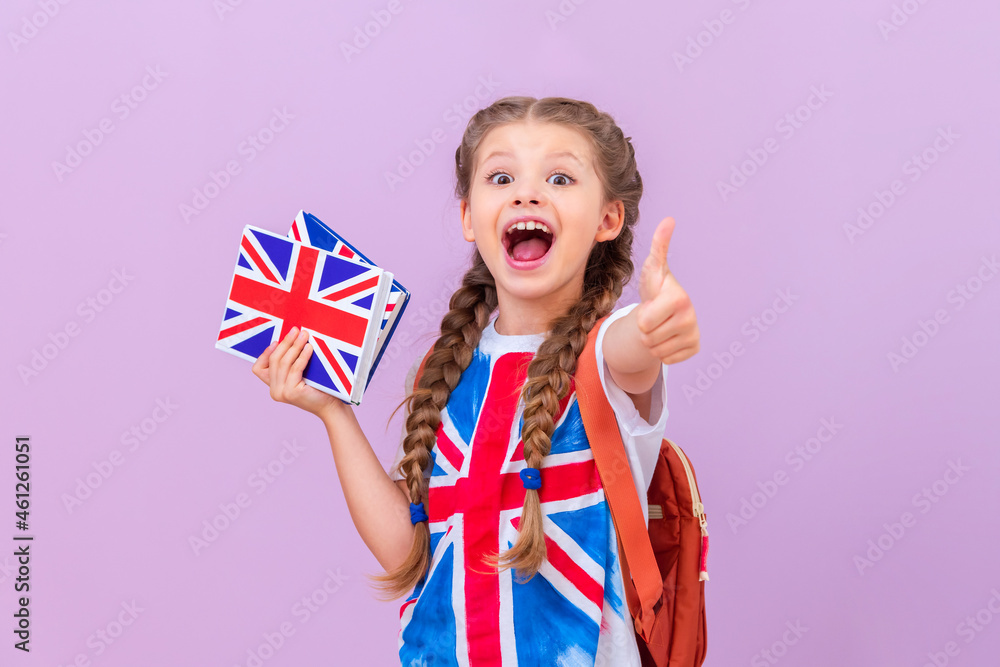 A student, holding books on learning English in her hands and smiling shows her thumb to the top. Isolated background. - obrazy, fototapety, plakaty 