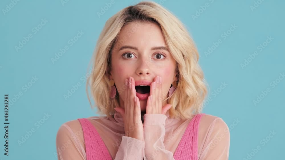 Close-up view of surprised woman covering her mouth in blue studio Close-up view of surprised woman covering her mouth in blue studio