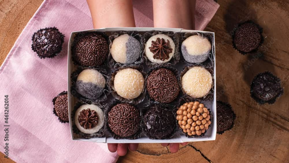 A child's hand holding a box with various types of gourmet brigadeiro. Typical sweet from Brazil. Brigadiers. Top view A child's hand holding a box with various types of gourmet brigadeiro. Typical sweet from Brazil. Brigadiers. Top view