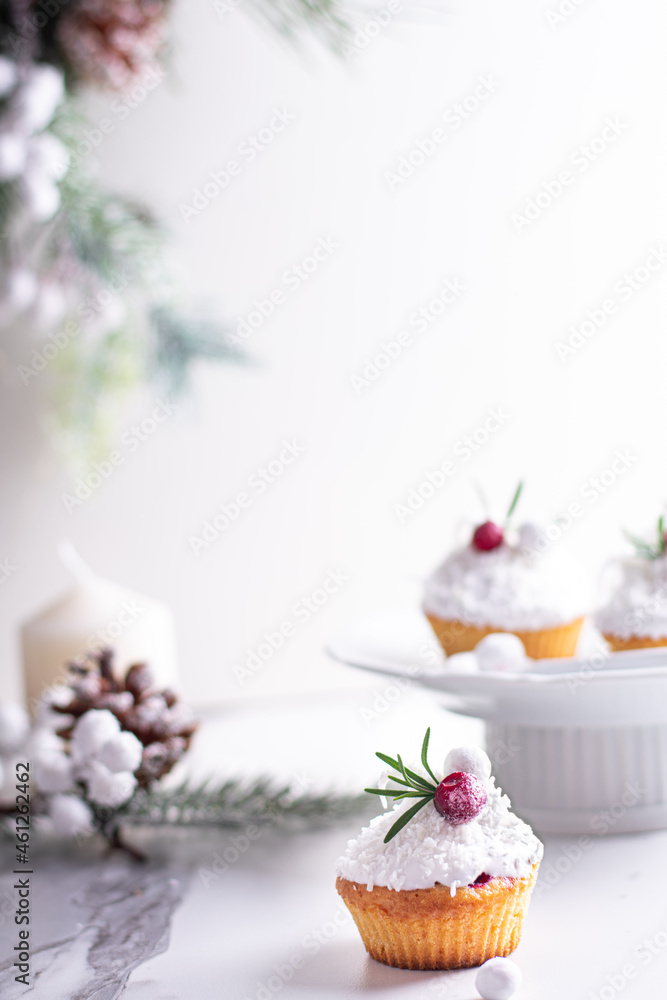 Christmas cupcakes with vanilla frosting, cranberries and rosemary on white background. Vertical