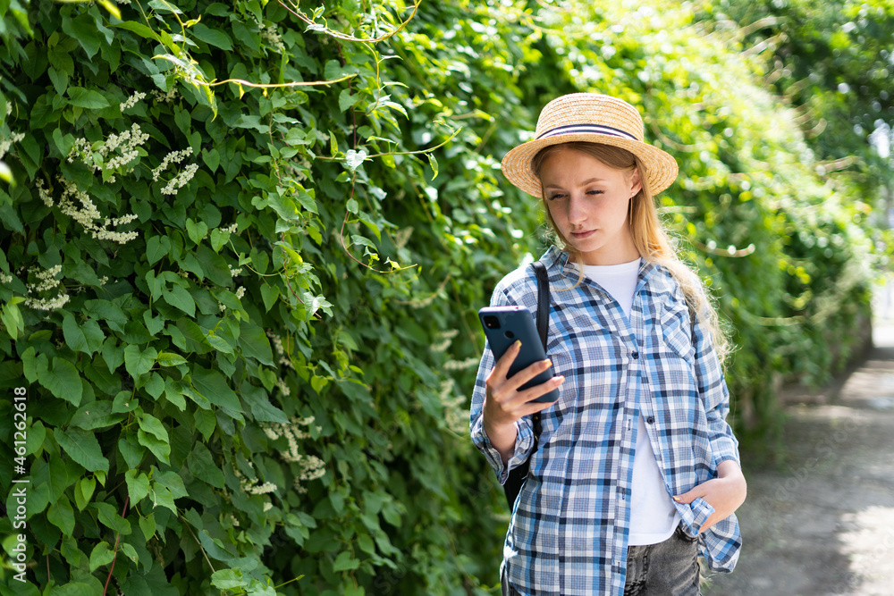 Girl tourist on a journey records a video on a mobile phone while standing near the greenery in the background. A female traveler is streaming