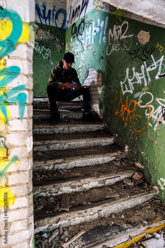 Young boy sitting on stairs in ruined building and using smarthphone