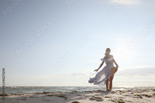 Woman in dress with straw hat walking by sea on sunny day